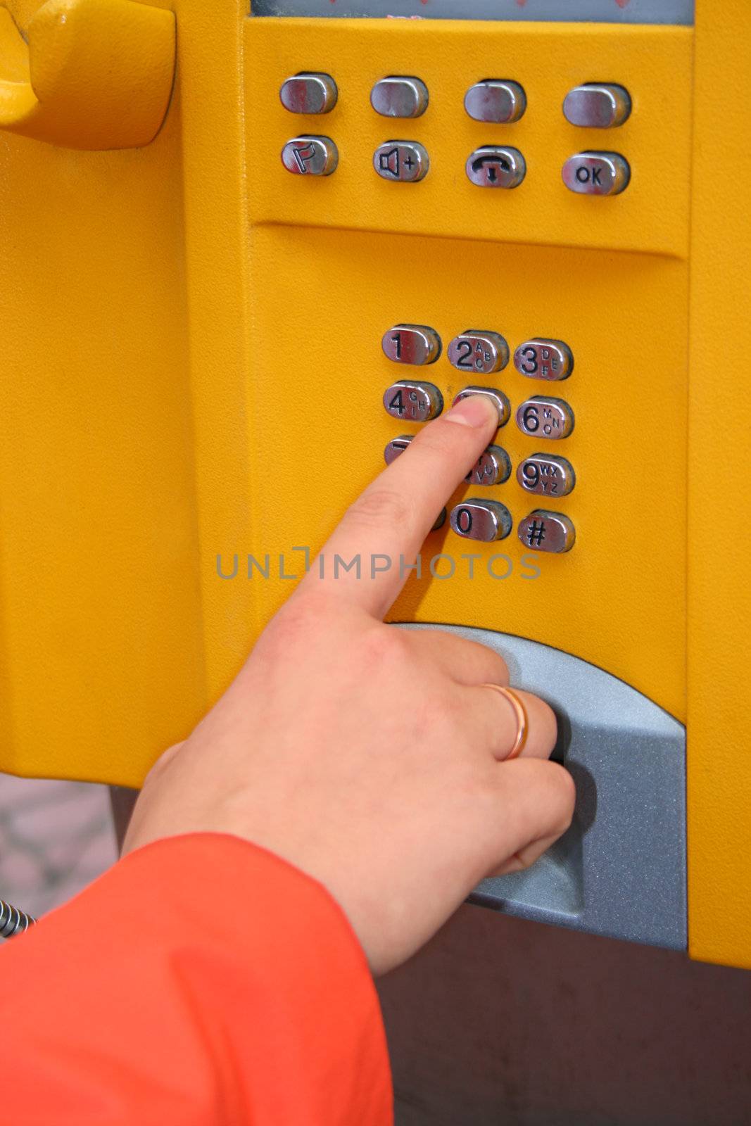 Woman's hand pressing the key on the public telephone's keyboard
