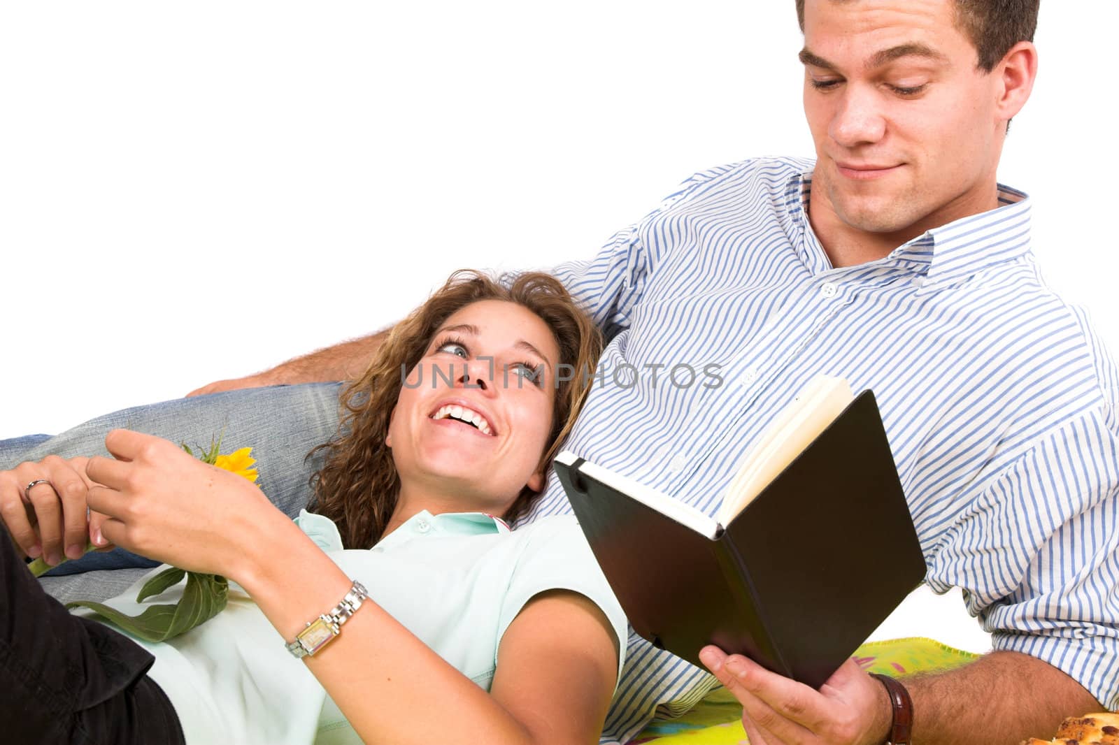 Man reading a book while on a picnic while his girlfriend is lying on his lap