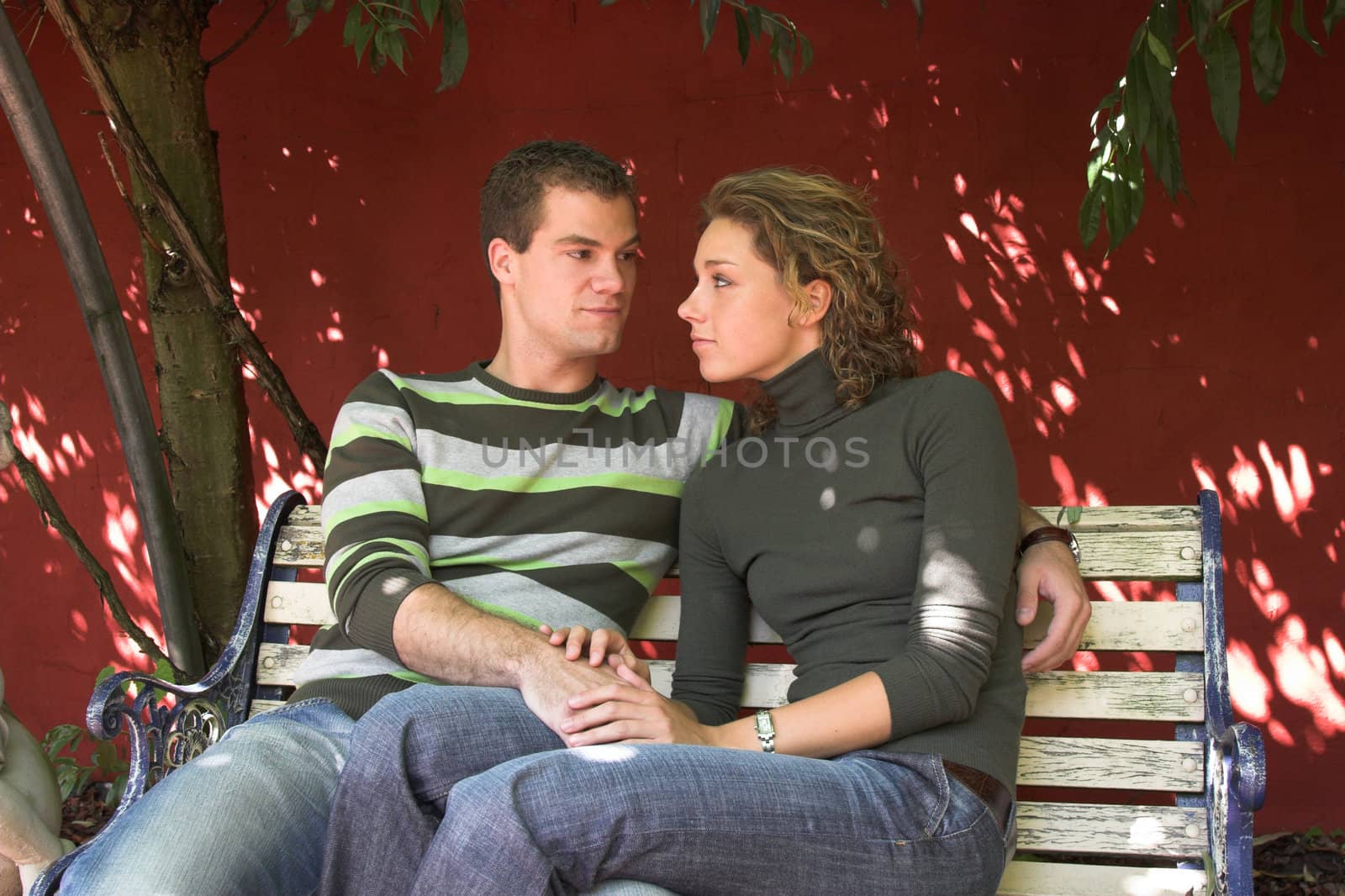 Lovely young couple looking at eachother while sitting on a bench in the garden