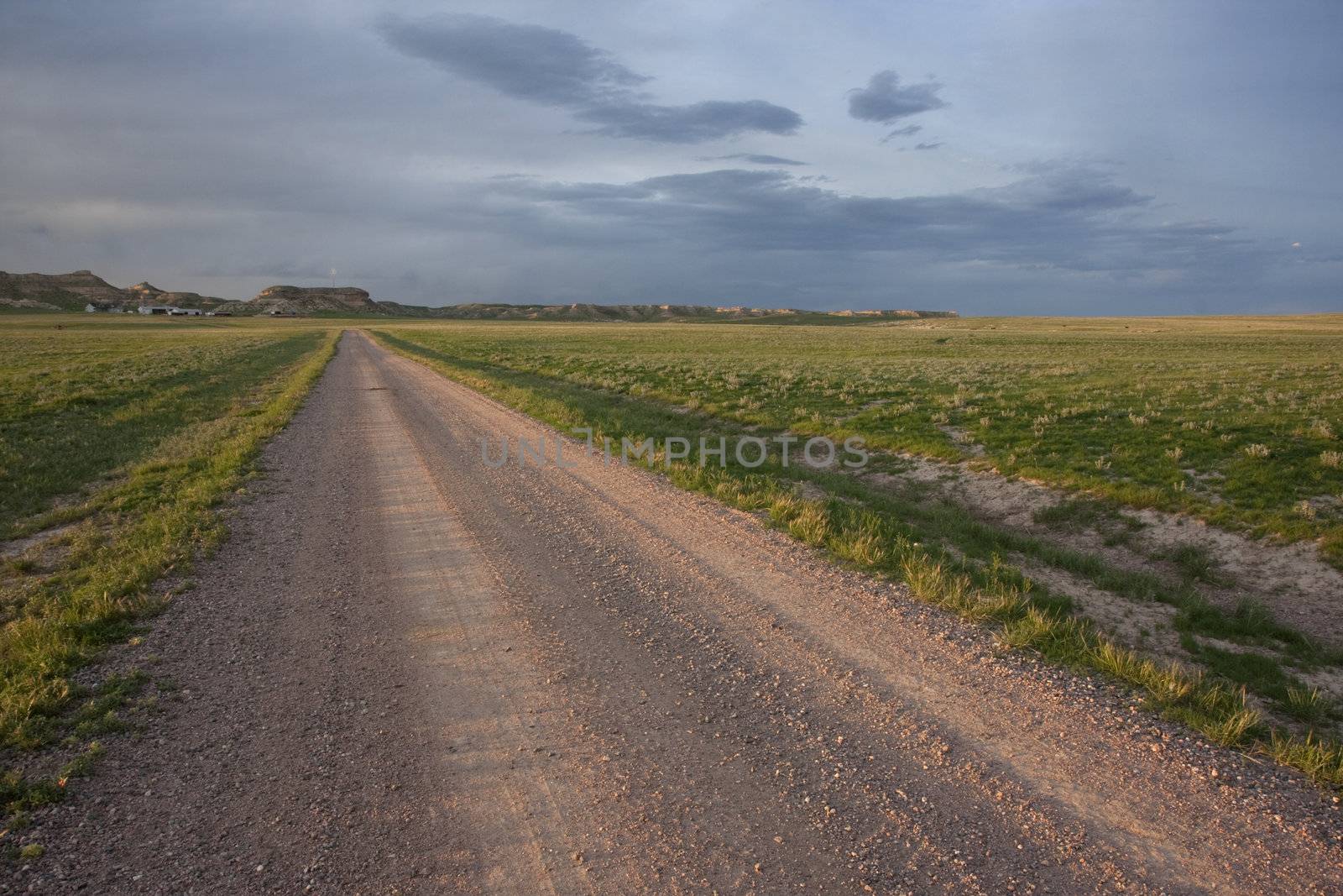 dirt farm road in Pawnee Grassland, northern Colorado, high cliffs. farm buildings and wind turbine at horizon