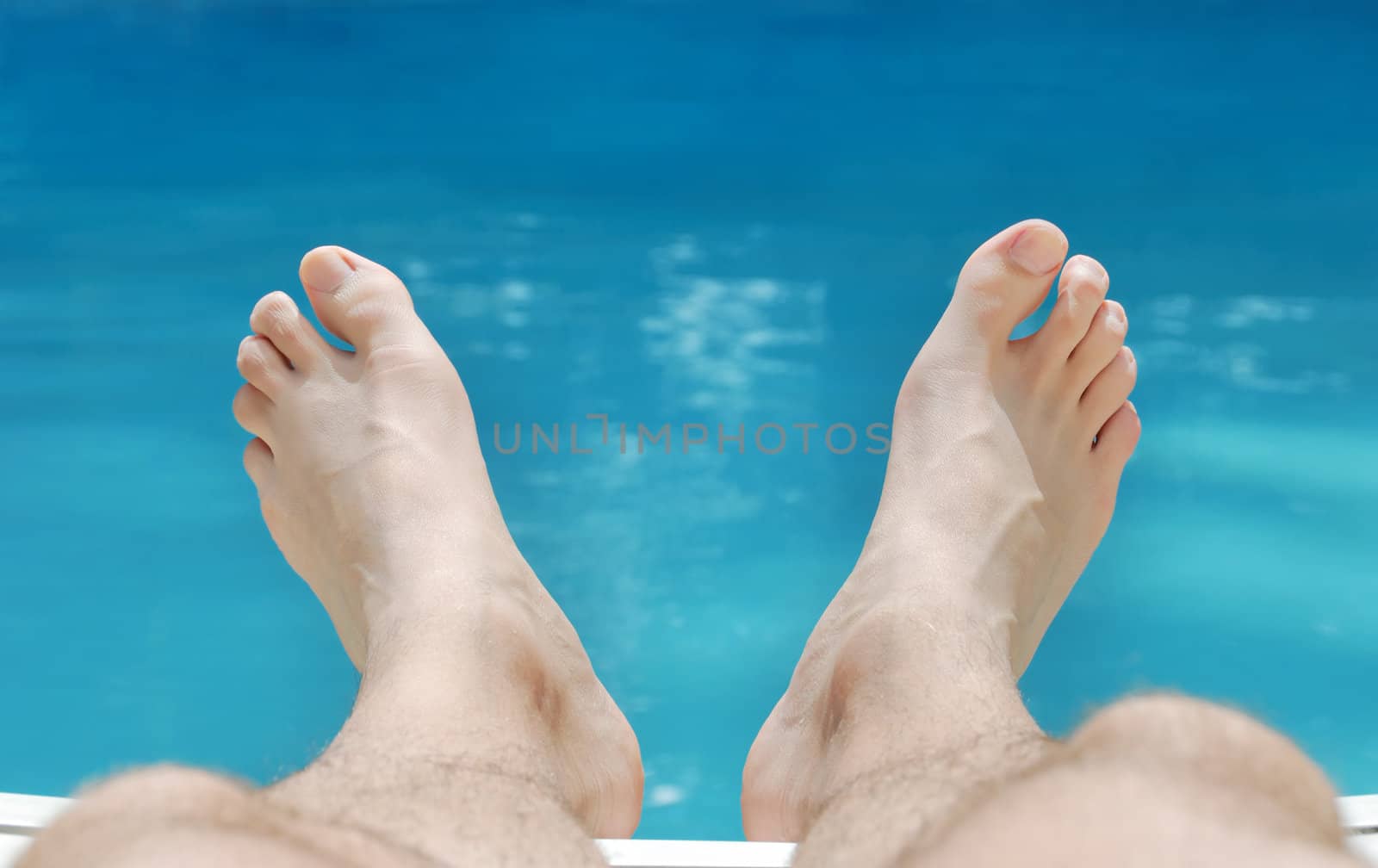 Two feet relaxing in sunlight with swimming pool water in the background.
