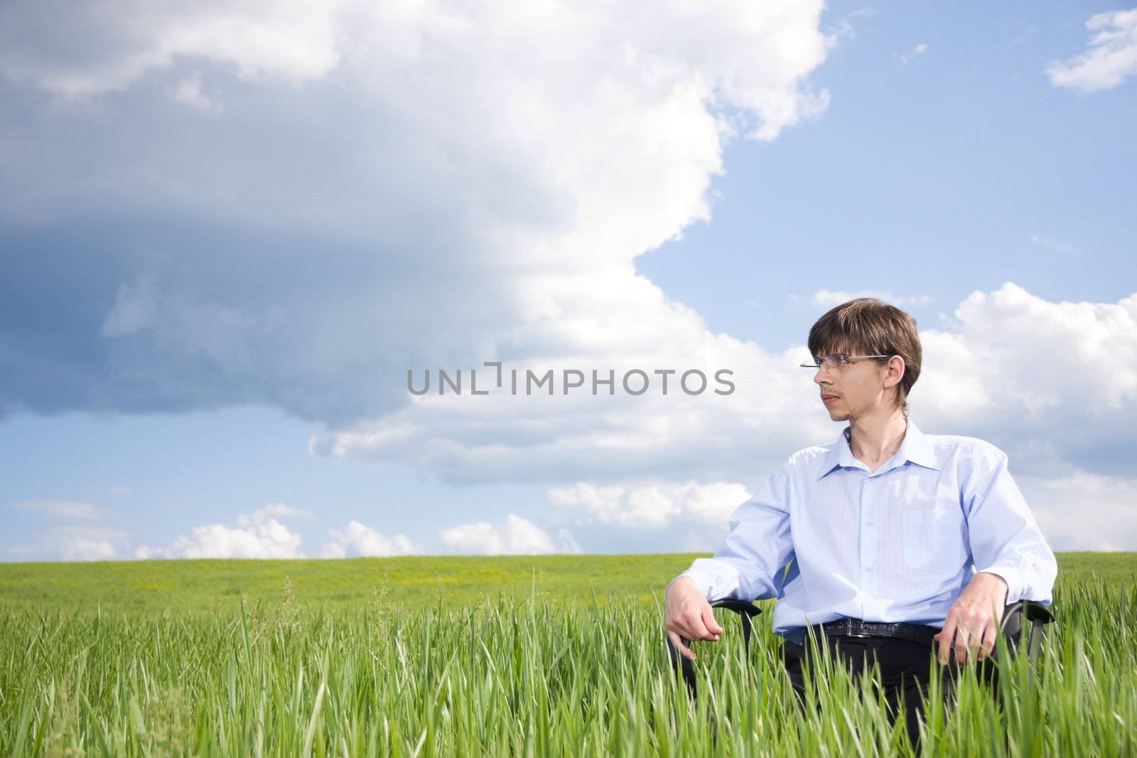 Businessman sitting on green grassland under blue sky