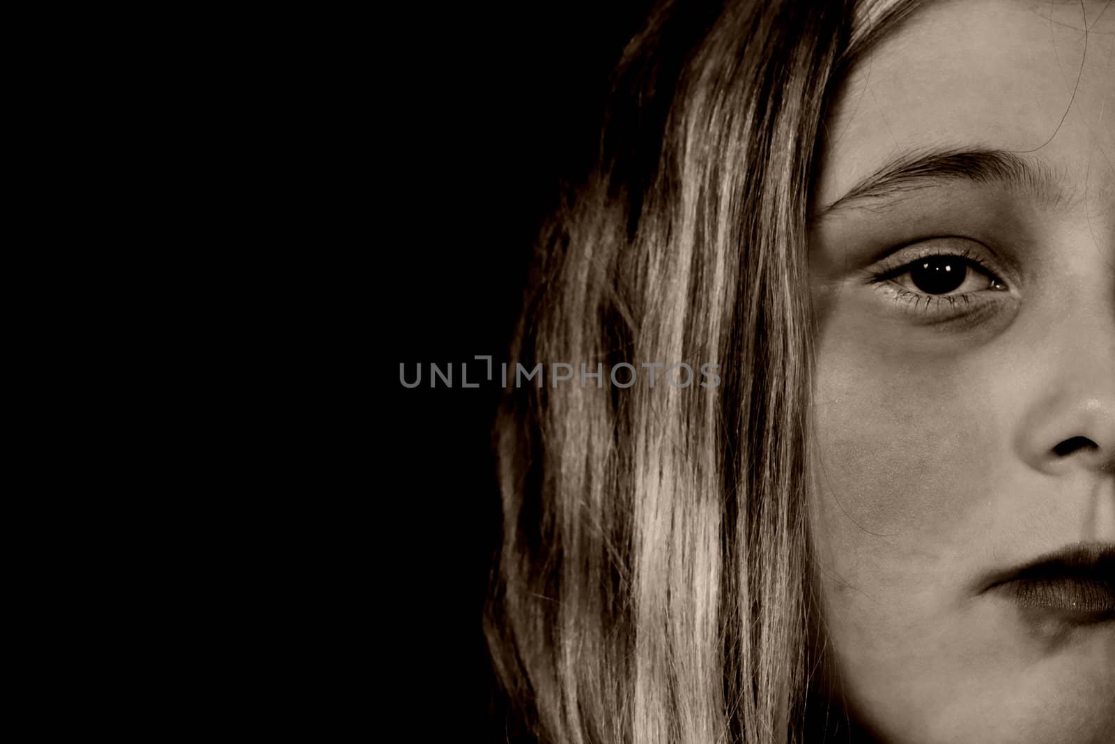 A young girl looking sullen because of child abuse and depression, isolated against a black background