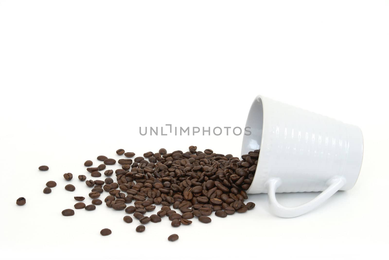 A cup of coffee beans has spilled onto a white background.
