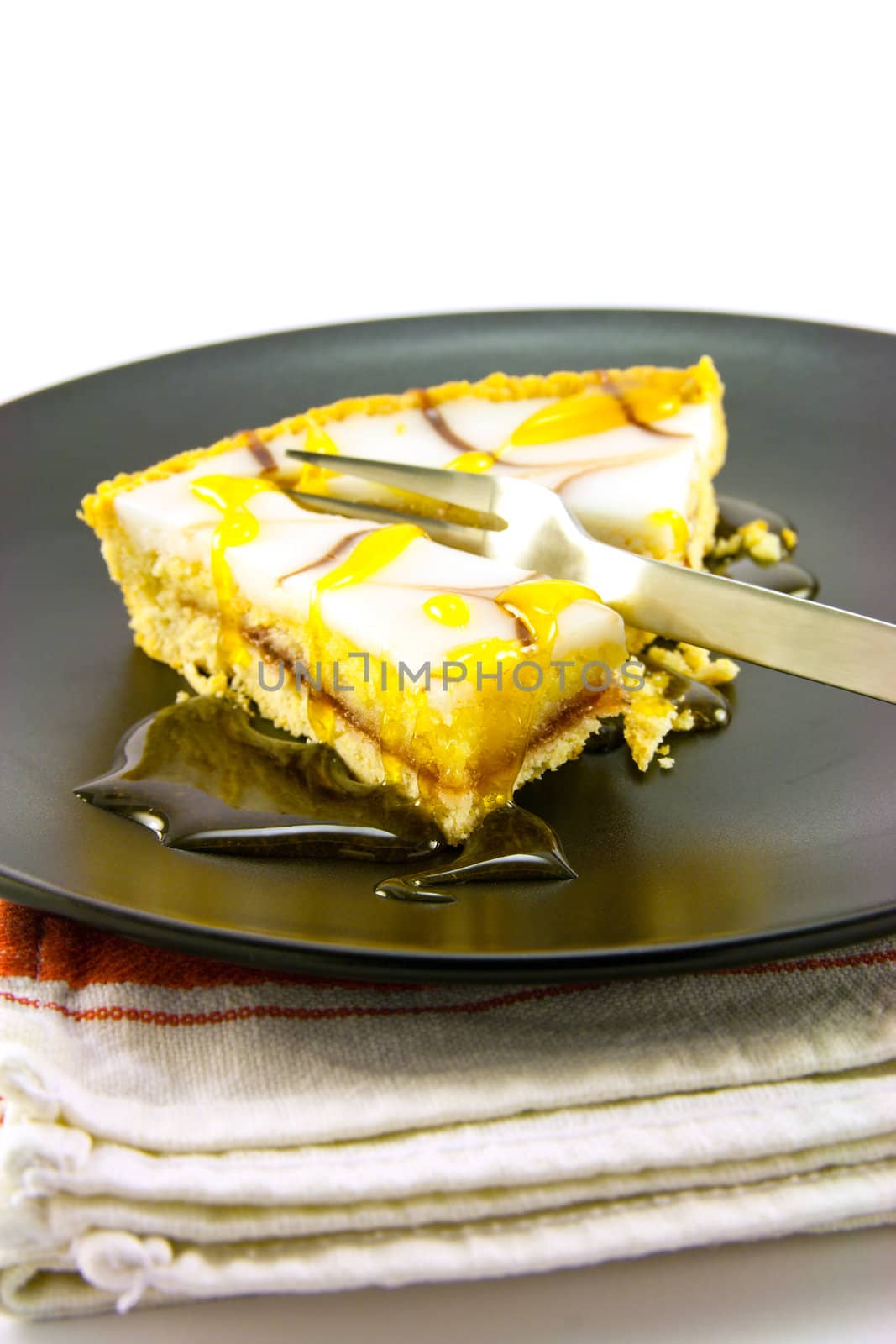 delicious looking iced bakewell tart on a black plate with a treacle drizzle and a fork on a plain background