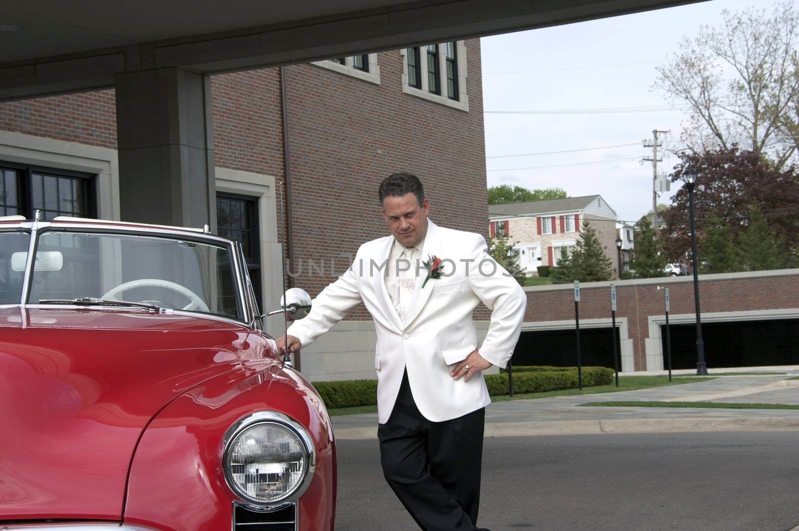 A sharp dressed man standing next to a classic convertible car holding the door.
