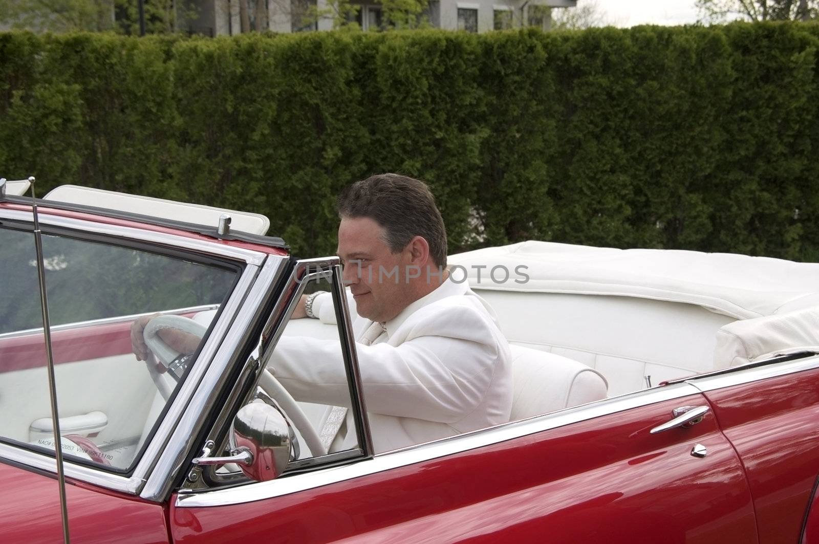 A sharp dressed man driving an old classic convertible car.