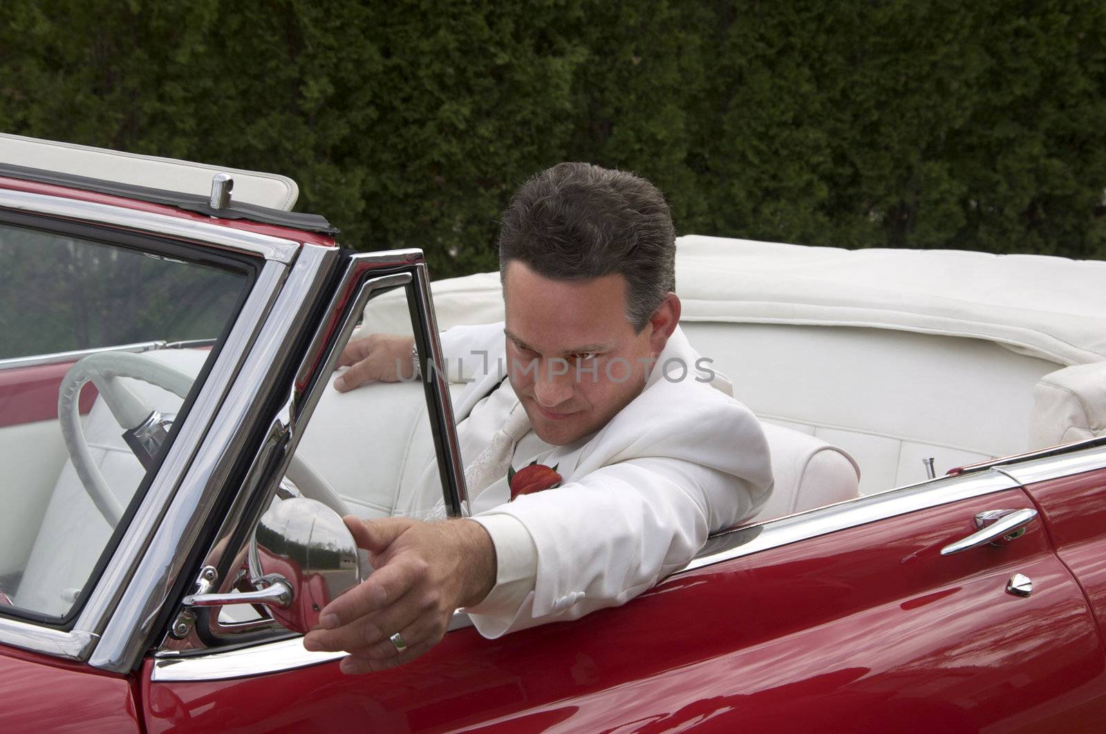 A well dressed man in a classic red convertible.
