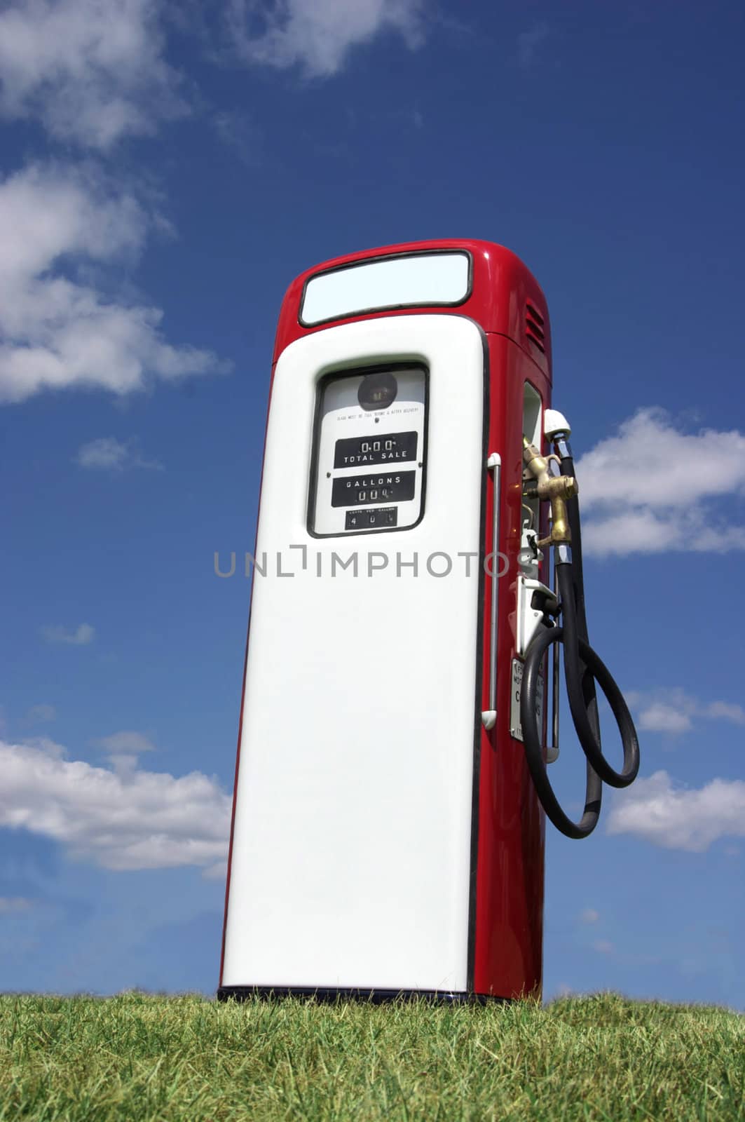 A vintage antique Gasoline fuel pump sitting on a grassy hill against the blue sky.