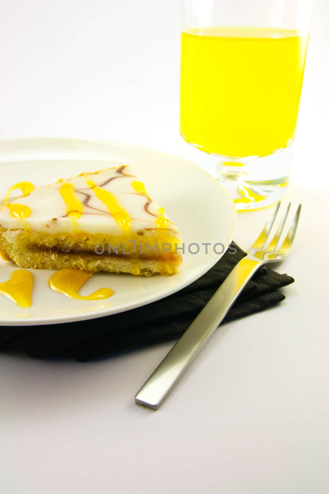 delicious looking iced bakewell tart on a black plate with a treacle drizzle and a fork on a plain background