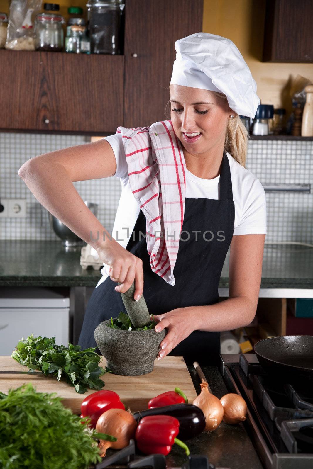 Pretty blond female chef using a pestle and mortar to crunch herbs