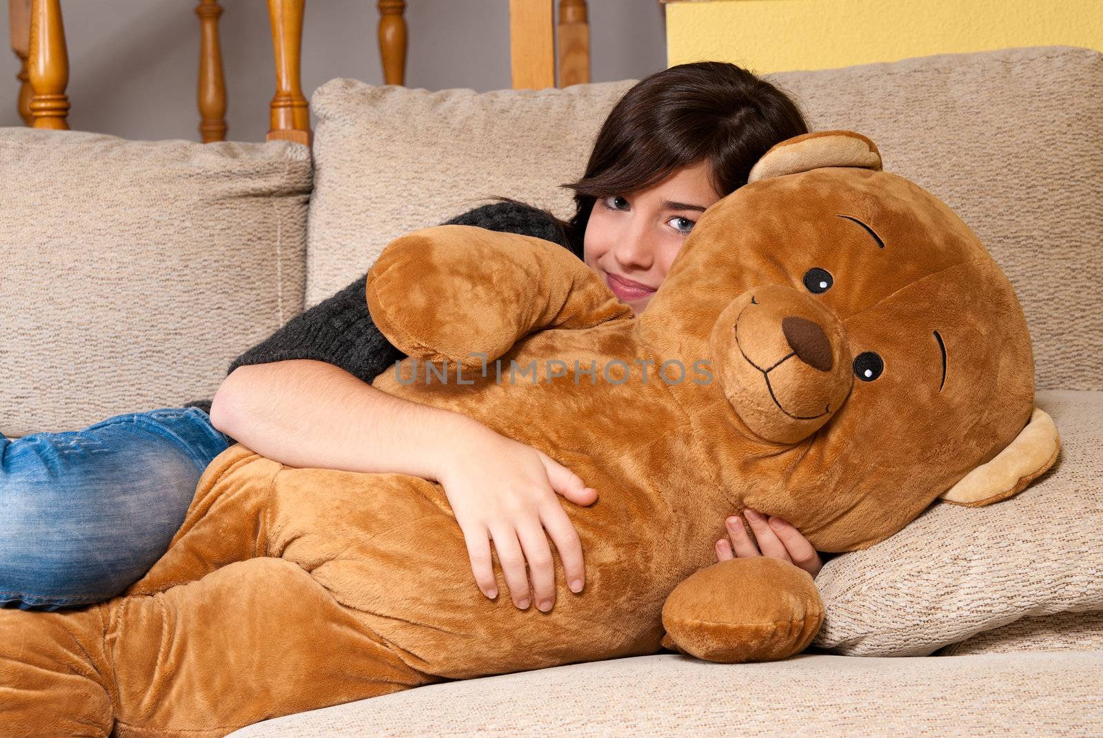 Young woman embracing teddy bear lying on on sofa by dgmata