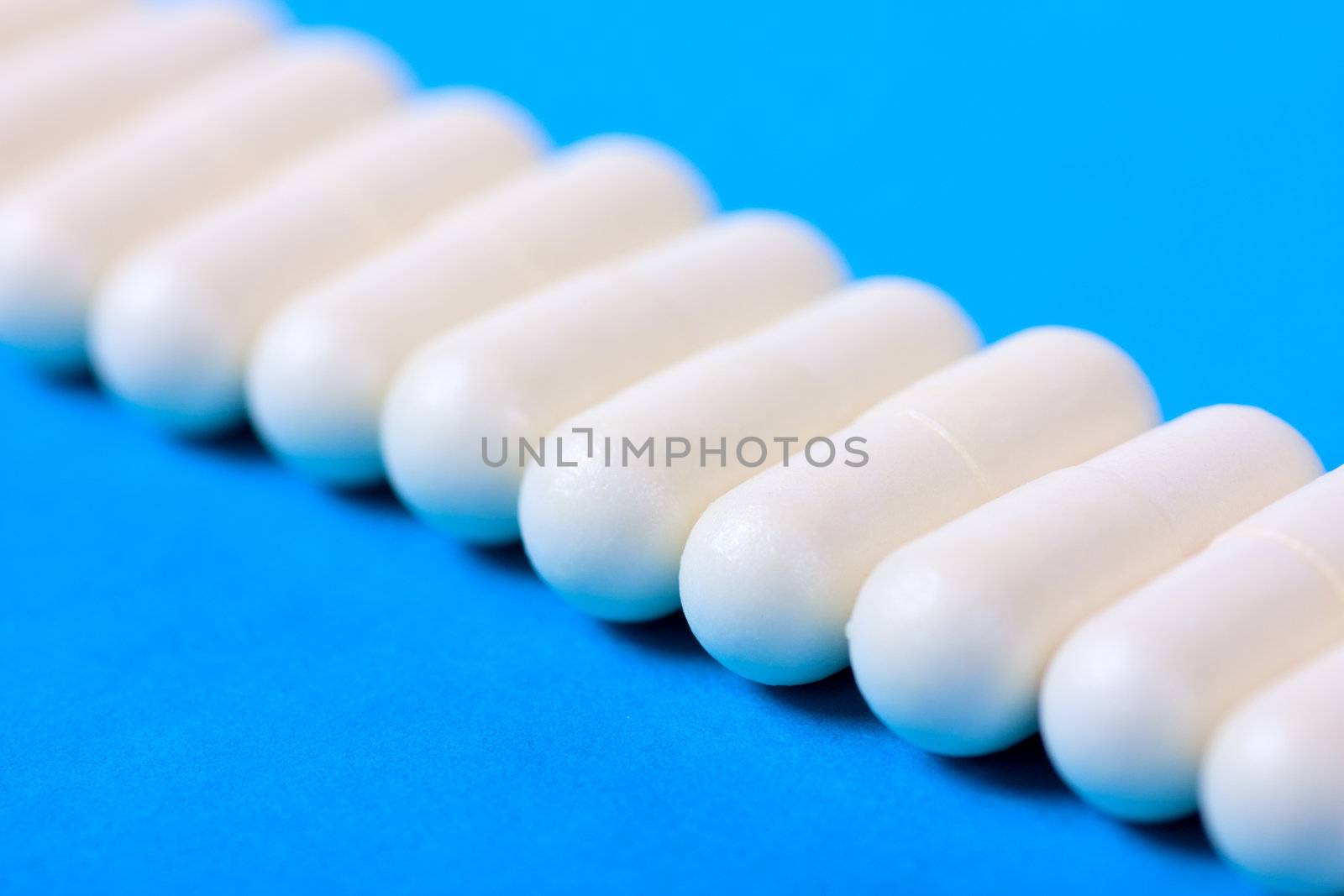 A row of white pilsl on a blue background. Macro view