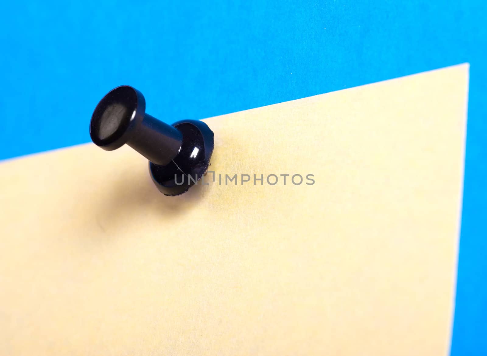 Yellow note on a blue background attached by black thumbtack