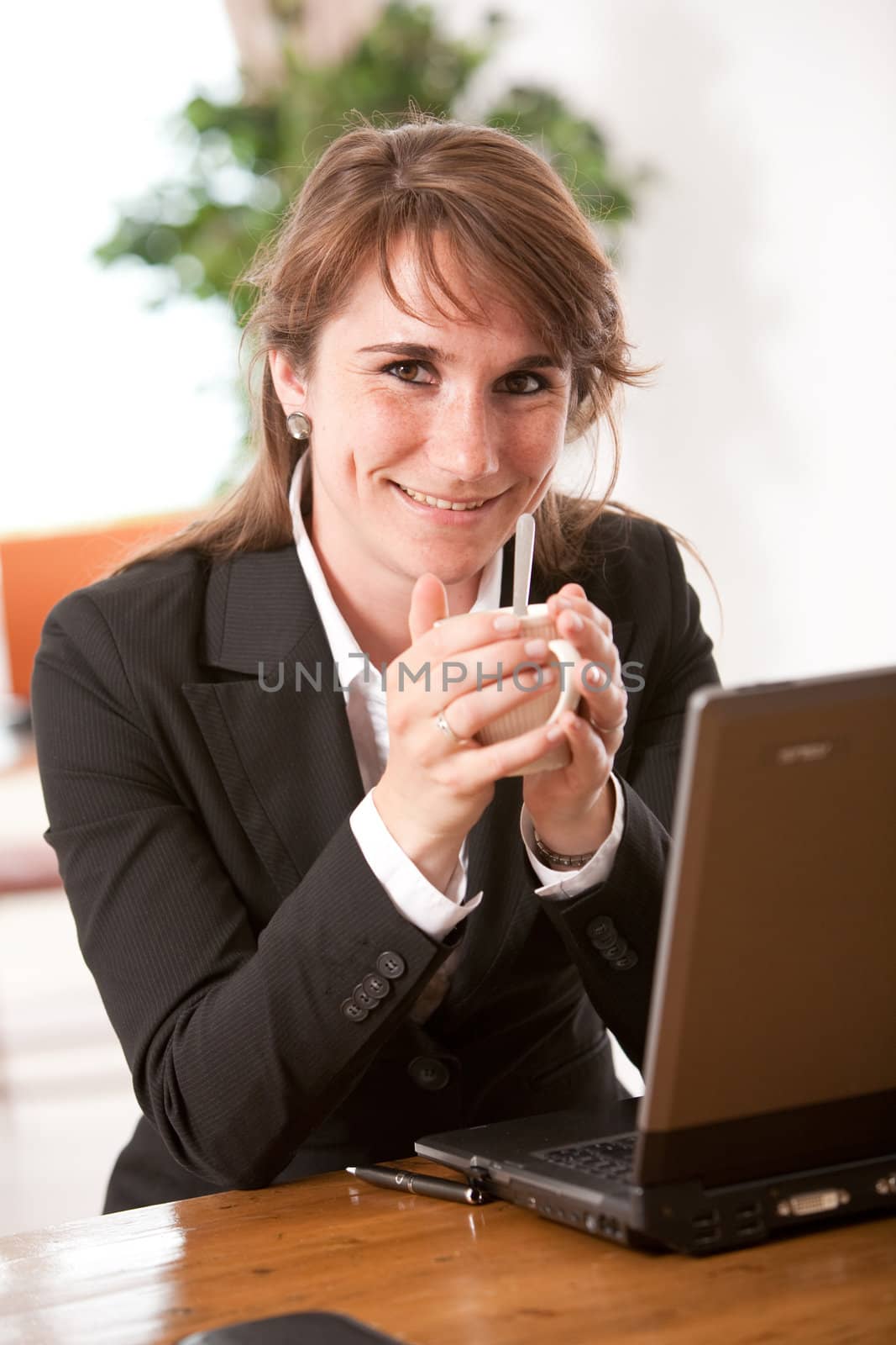 Pretty young woman in the office having her coffeebreak behind the laptop