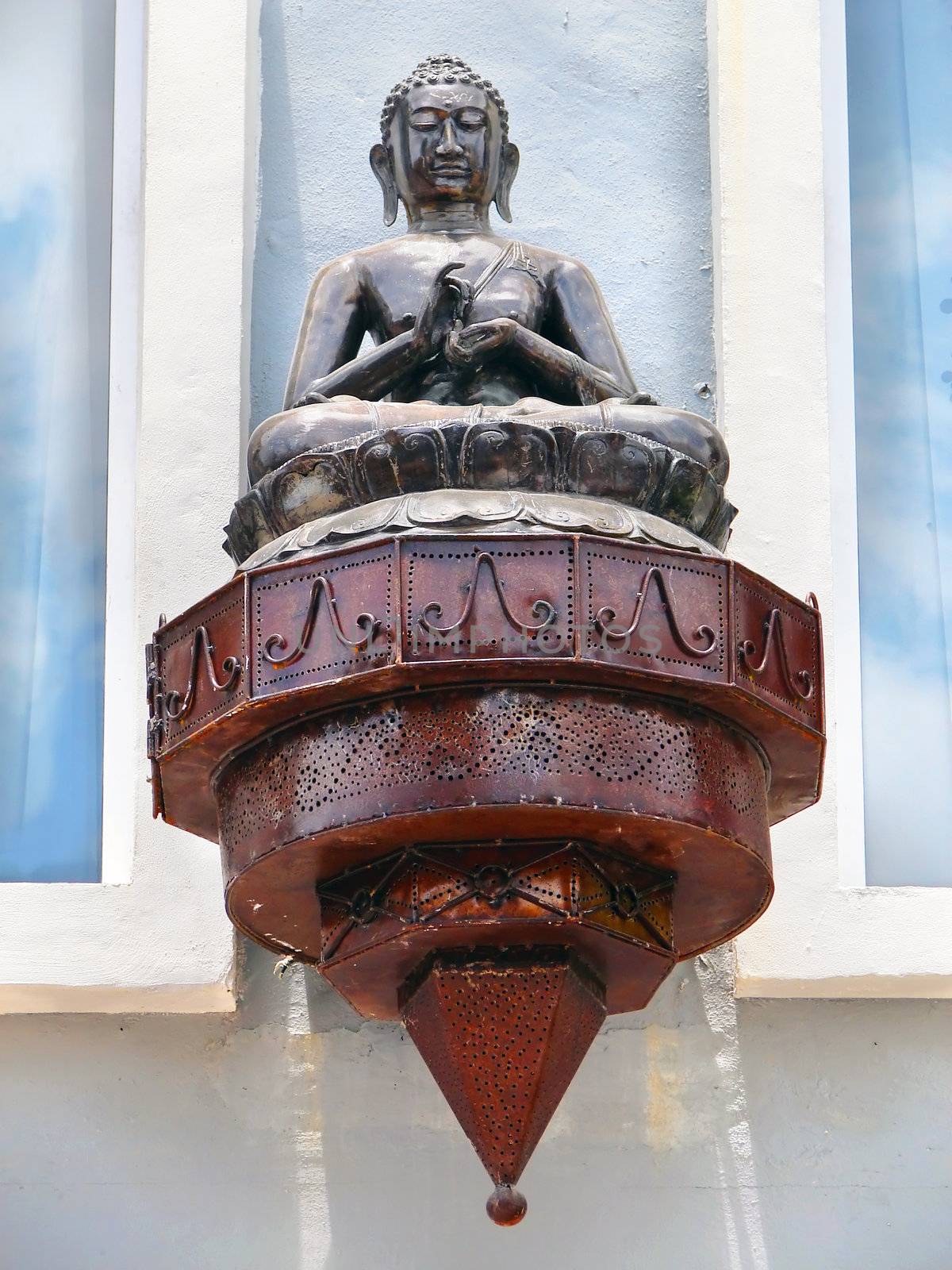 Cast iron and copper budha lantern against light blue stucco wall.