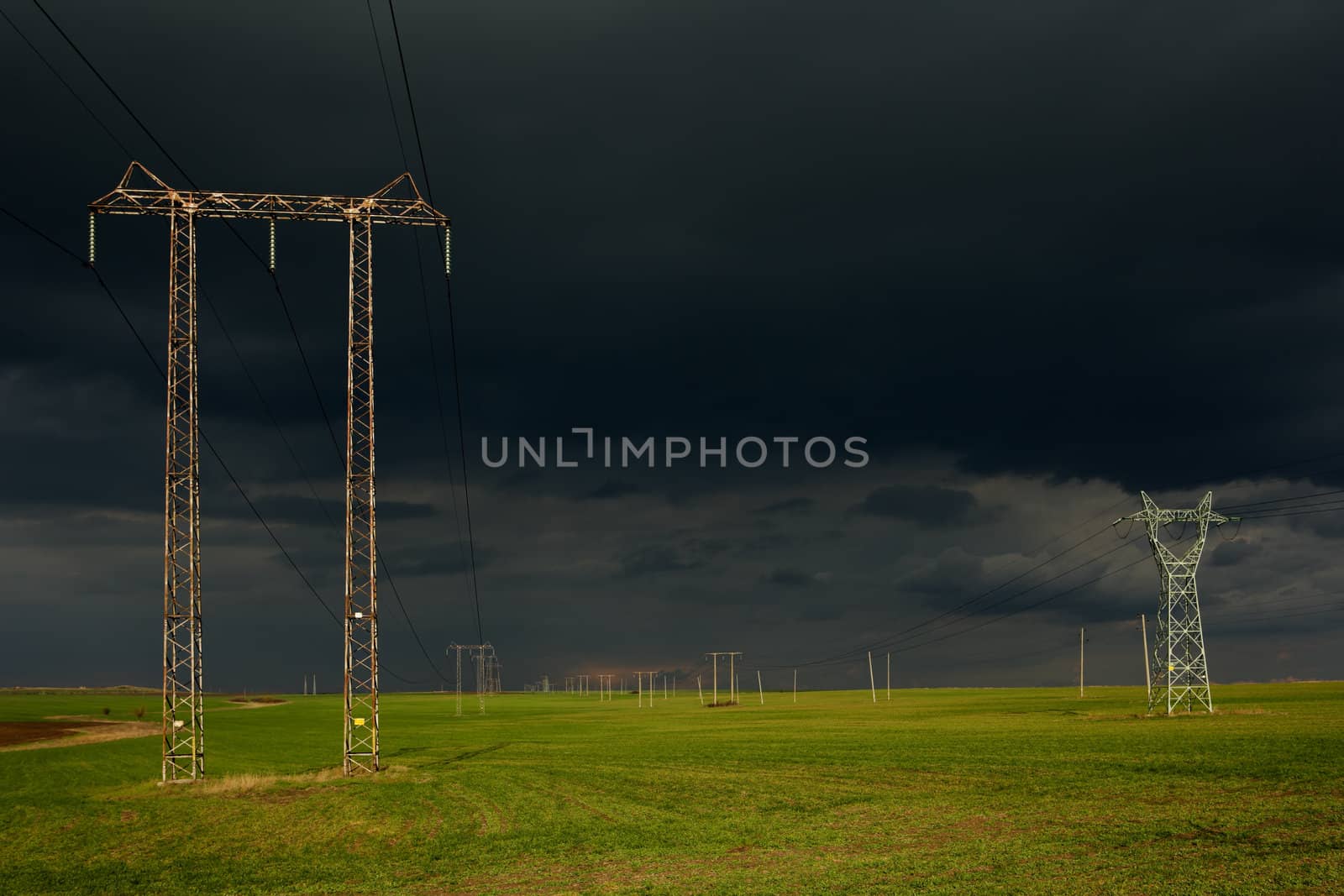 Landscape with dark storm clouds, green field and high voltage electricity poles