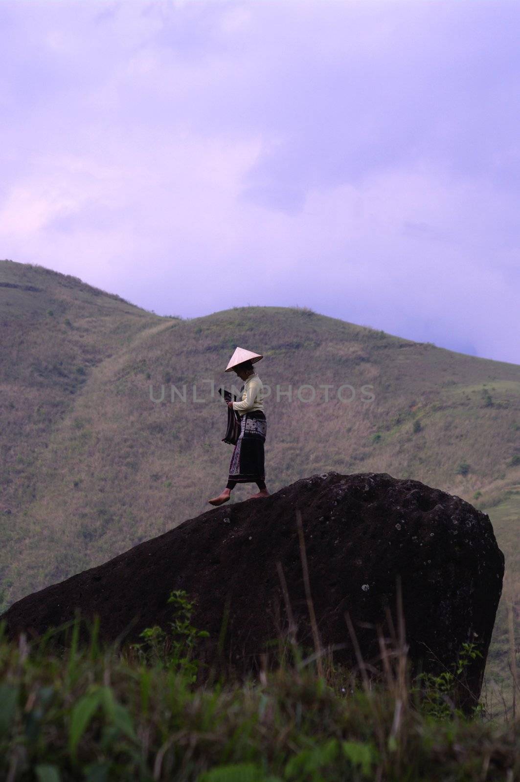 LU woman with her conical hat over his traditional headdress standing on a rock
