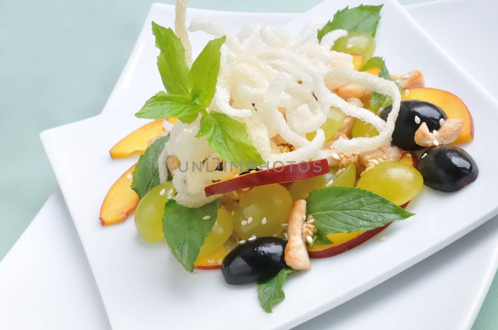 light salad with chicken, grapes, nectarines, sesame, with lemon dressing, decorated with fried rice noodles with mint