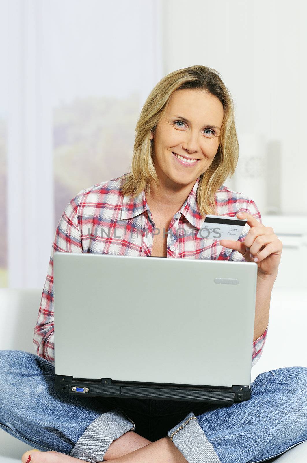Young woman sitting on sofa with computer and credit card