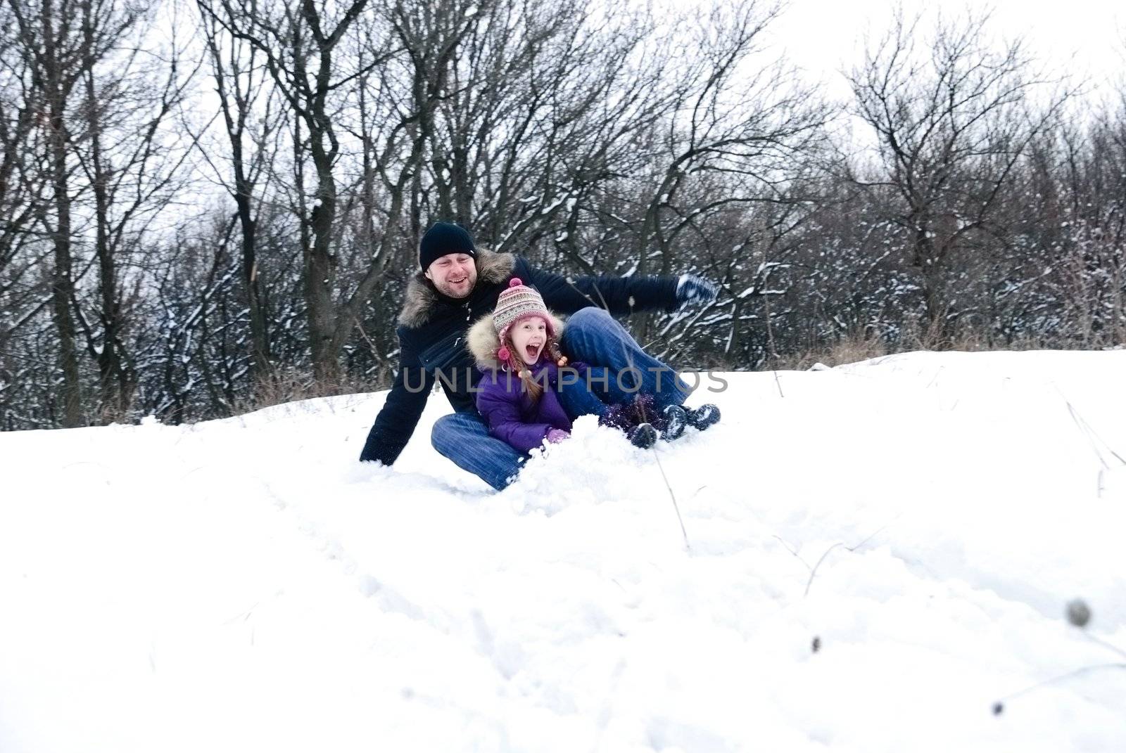 father and daughter riding on a sled in a winter woods