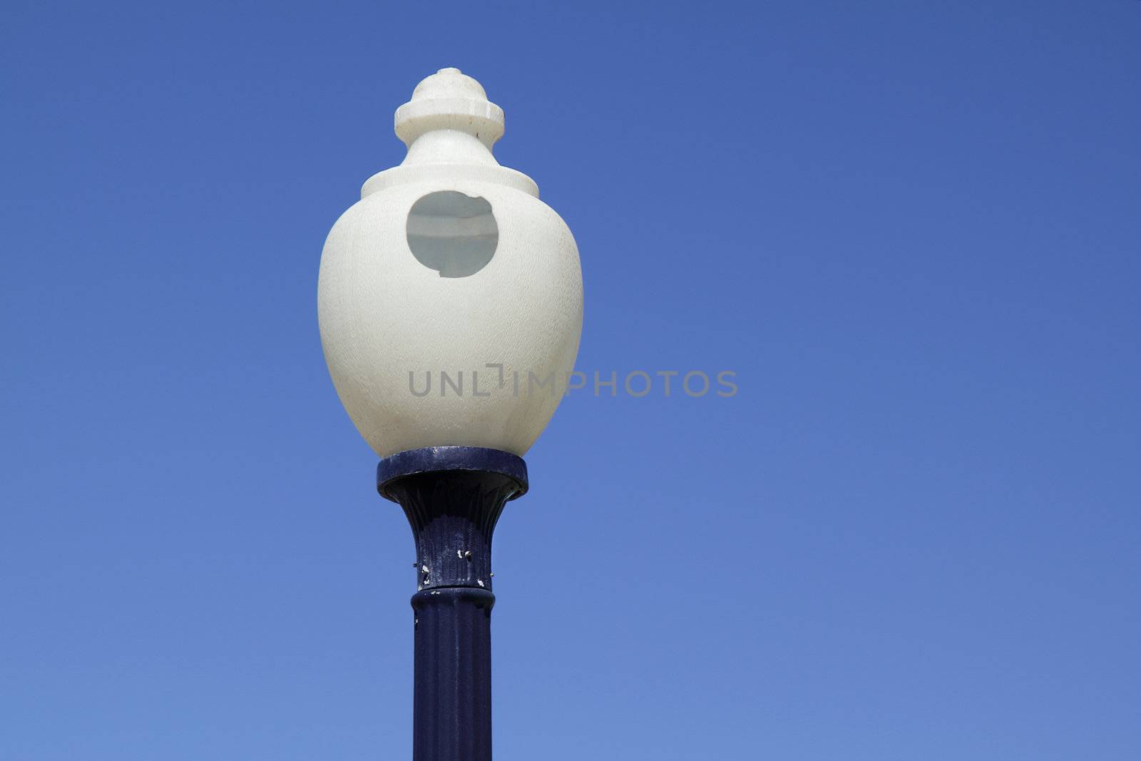 Round street lamp with a hole in the glass over blue sky