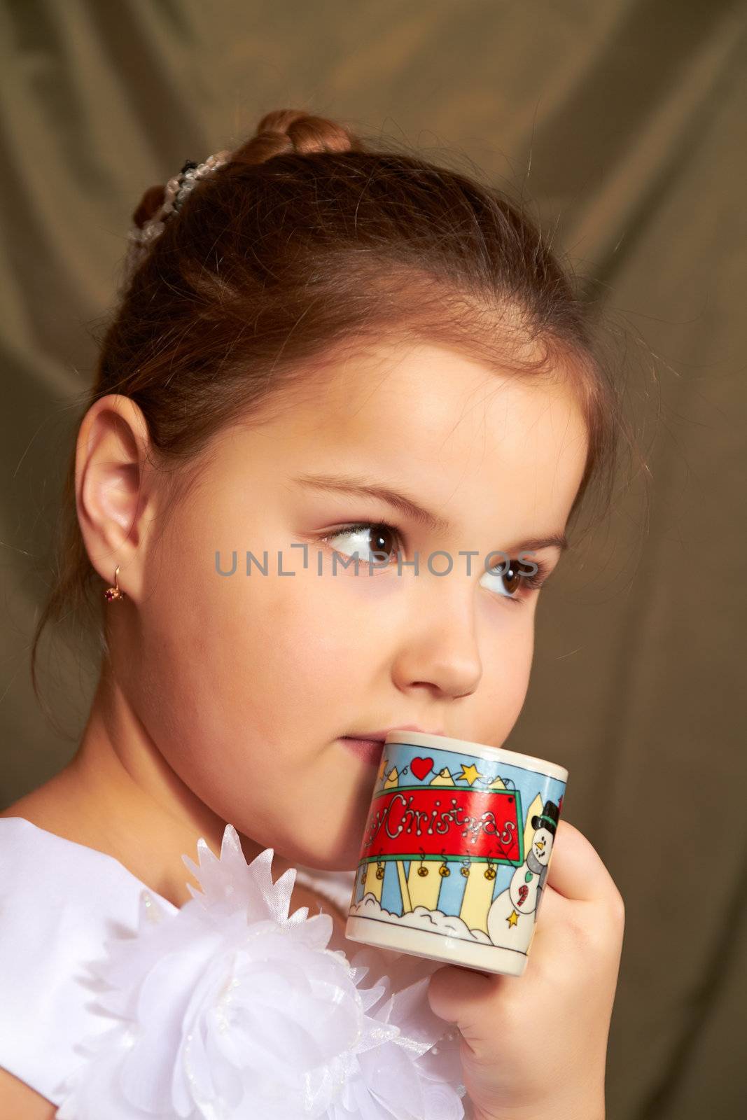 The little girl in a white dress drinks from a small cup.