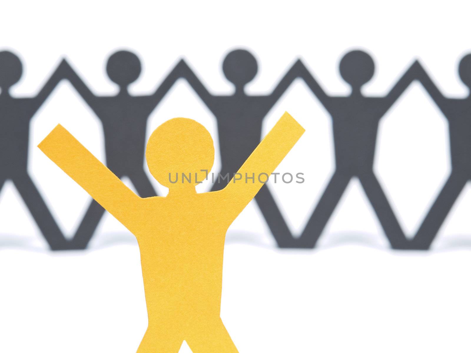 A yellow paper figure raising his arms. A paper man chain against the white background. Selective focus on the foreground.