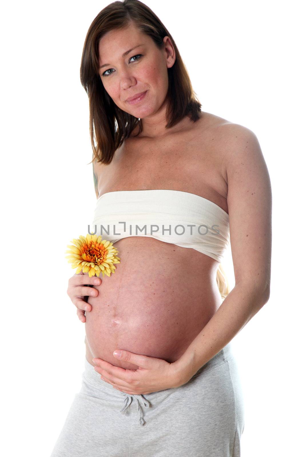 Smiling, very pregnant woman with baby belly looks toward the camera and holds a flower in your belly

