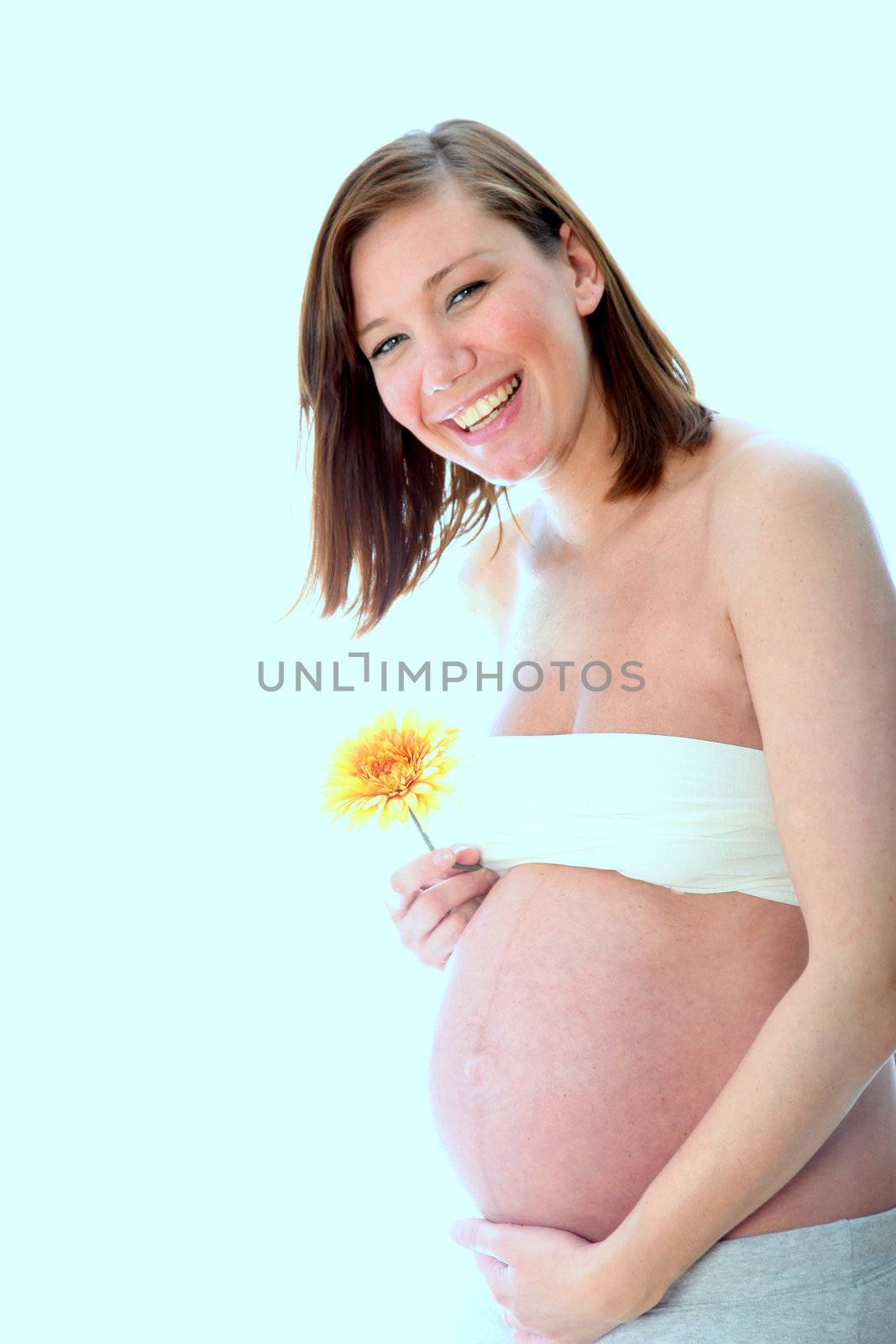pregnant, smiling, happy woman with a baby belly looks toward the camera and holding a flower
 