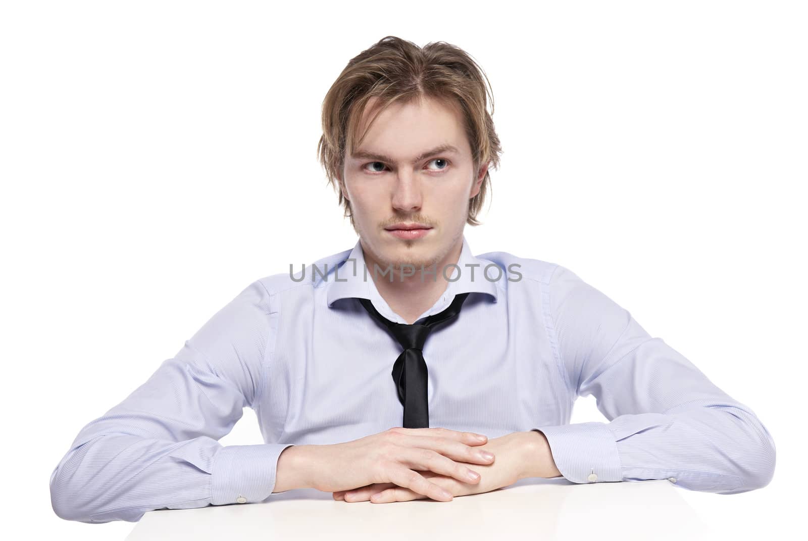 Young businessman, office worker or student sitting at funny small table. Studio photo, isolated.