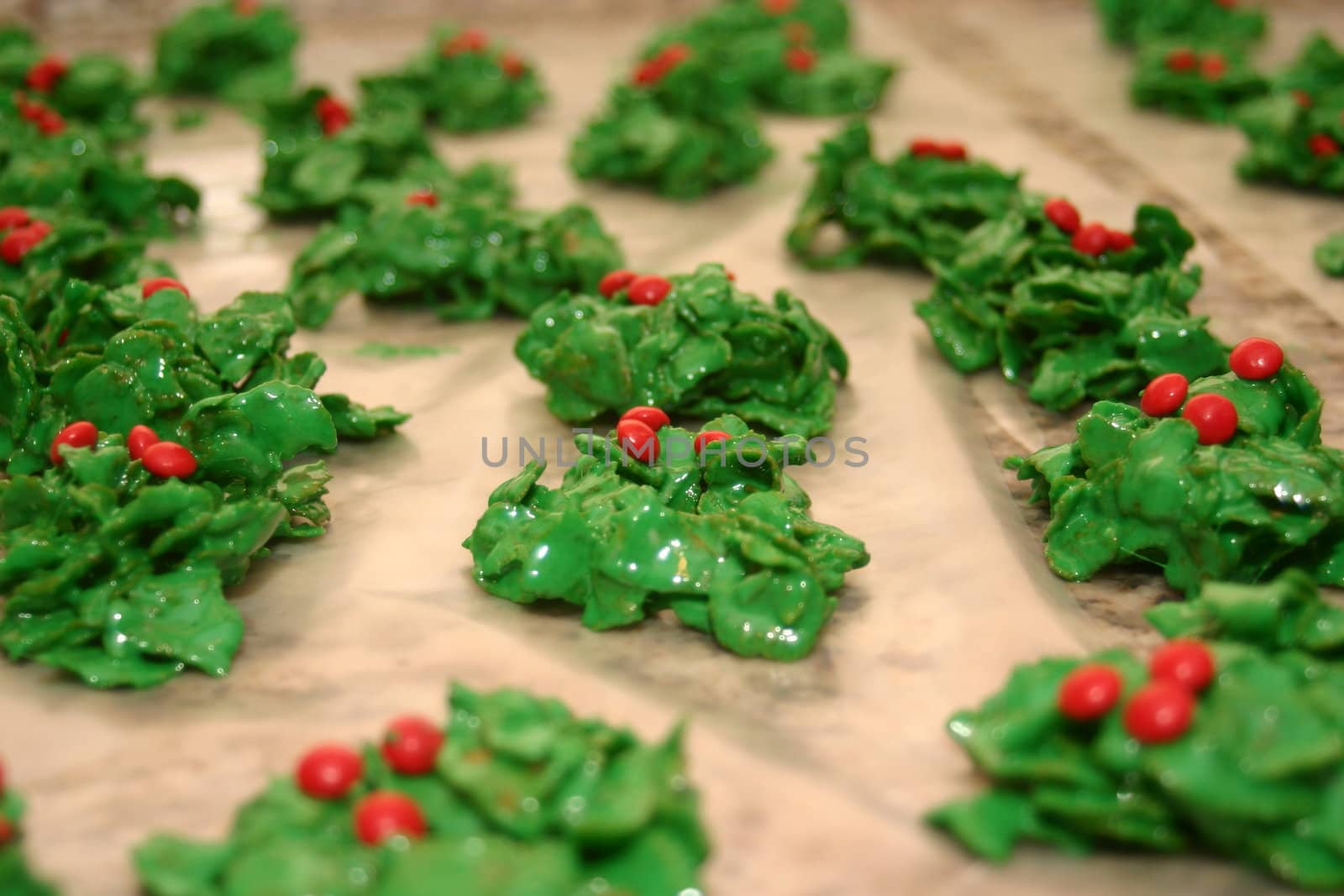 These are Christmas cookies that are made with marshmallows melted in butter, green food dye and breakfast flakes with red cinnamon candies on top spread out on wax paper.