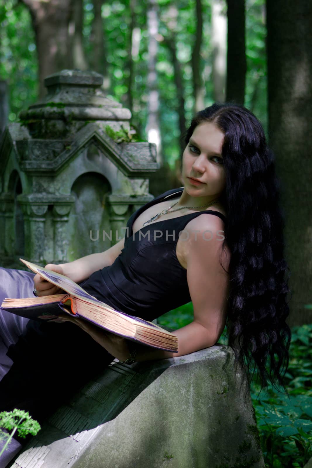 Gothic girl with old book posing on gravestone