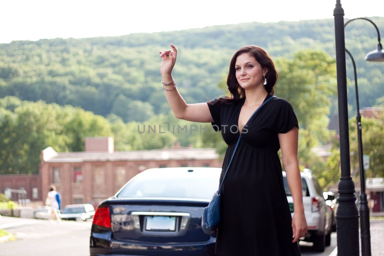 A beautiful brunette woman waving her arm tries to hail a cab at the side of the road in the city.