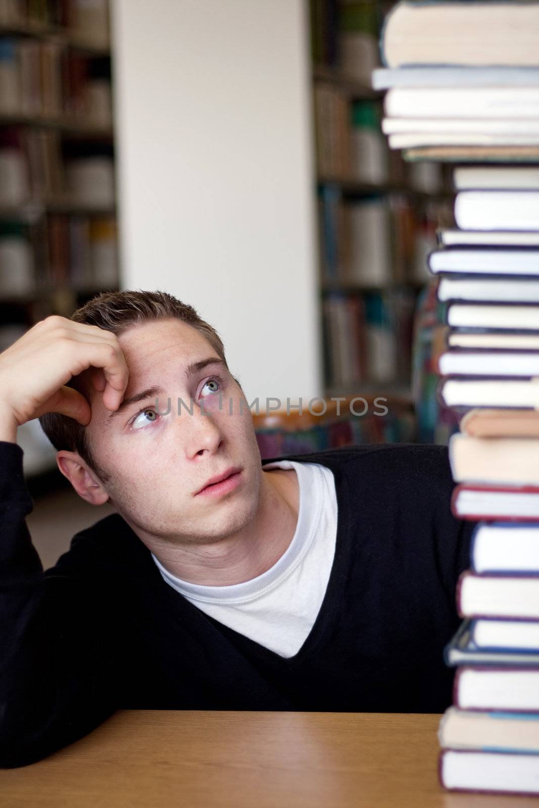 A frustrated and stressed out student looks up at the high pile of textbooks he has to go through to do his homework.