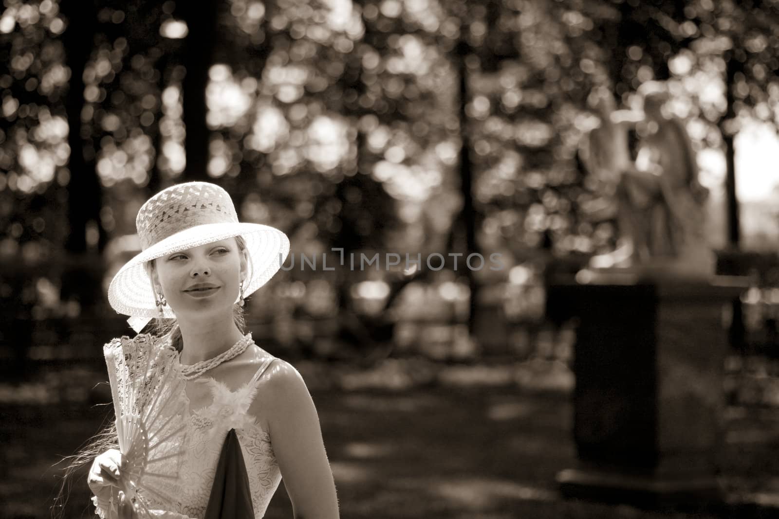 Young lady wearing white hat holding fan walking in park 