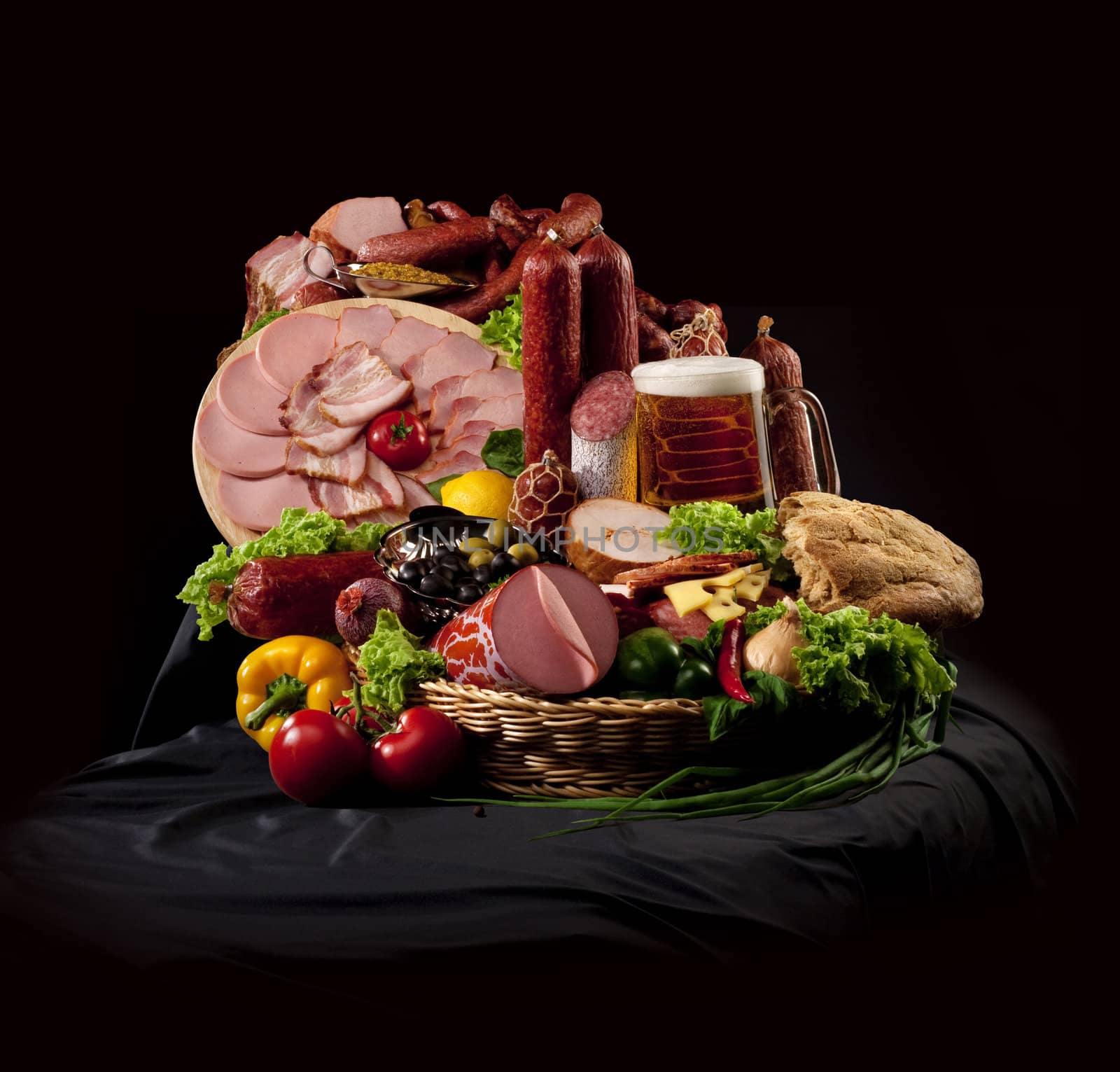 A composition of meat and vegetables with a pot full of beer on a black textile