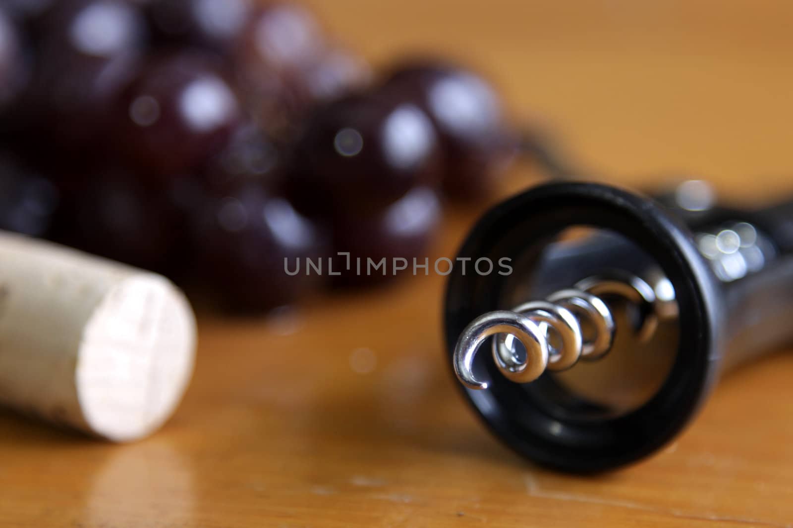 A cluster of juicy red grapes on a wood table, along with a corkscrew and a cork.
