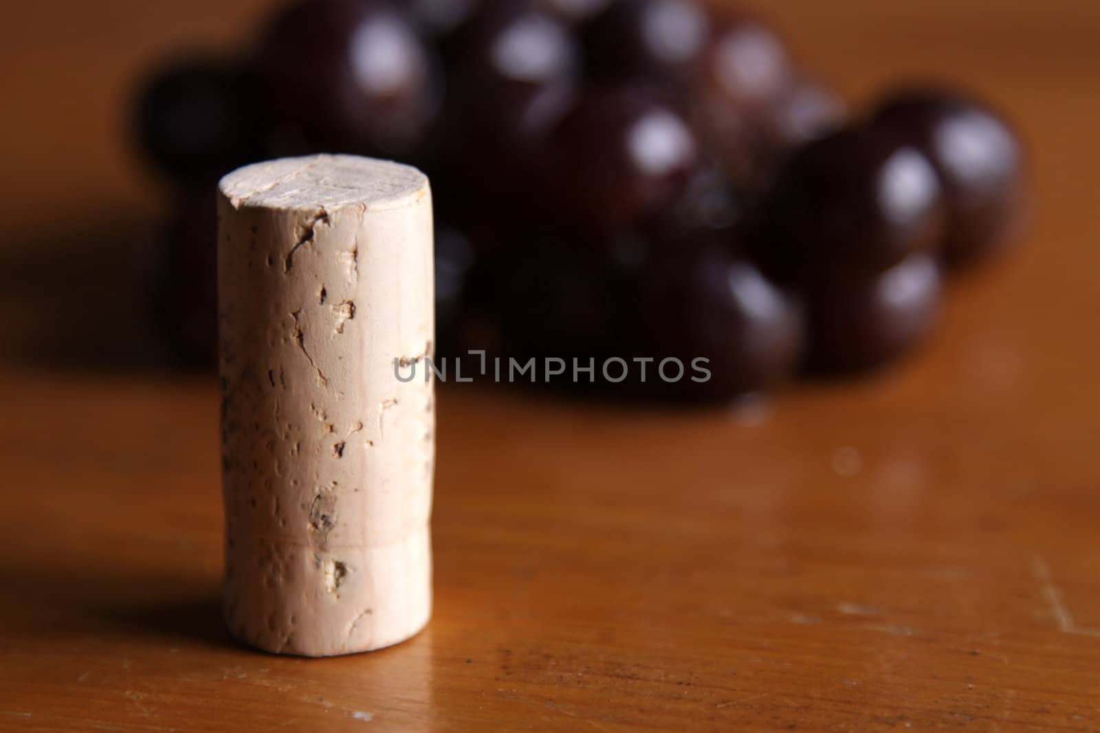 A wine bottle cork sitting in front of a cluster of grapes.