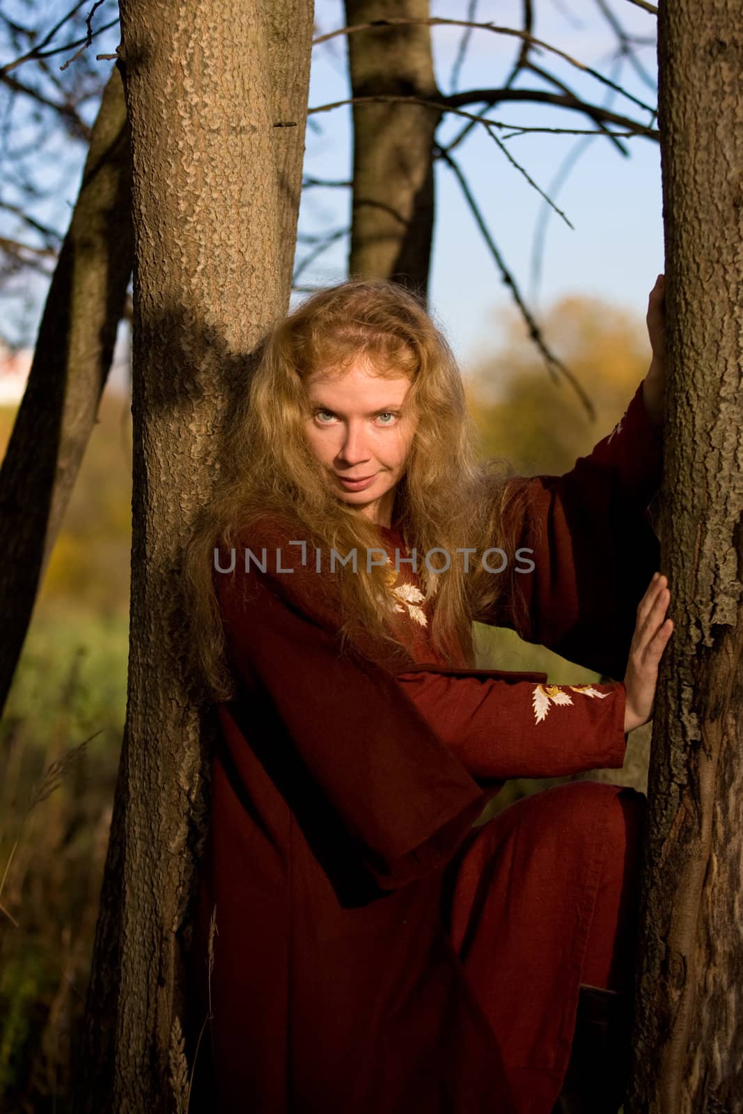 The blonde girl in medieval red dress in the autumn forest
