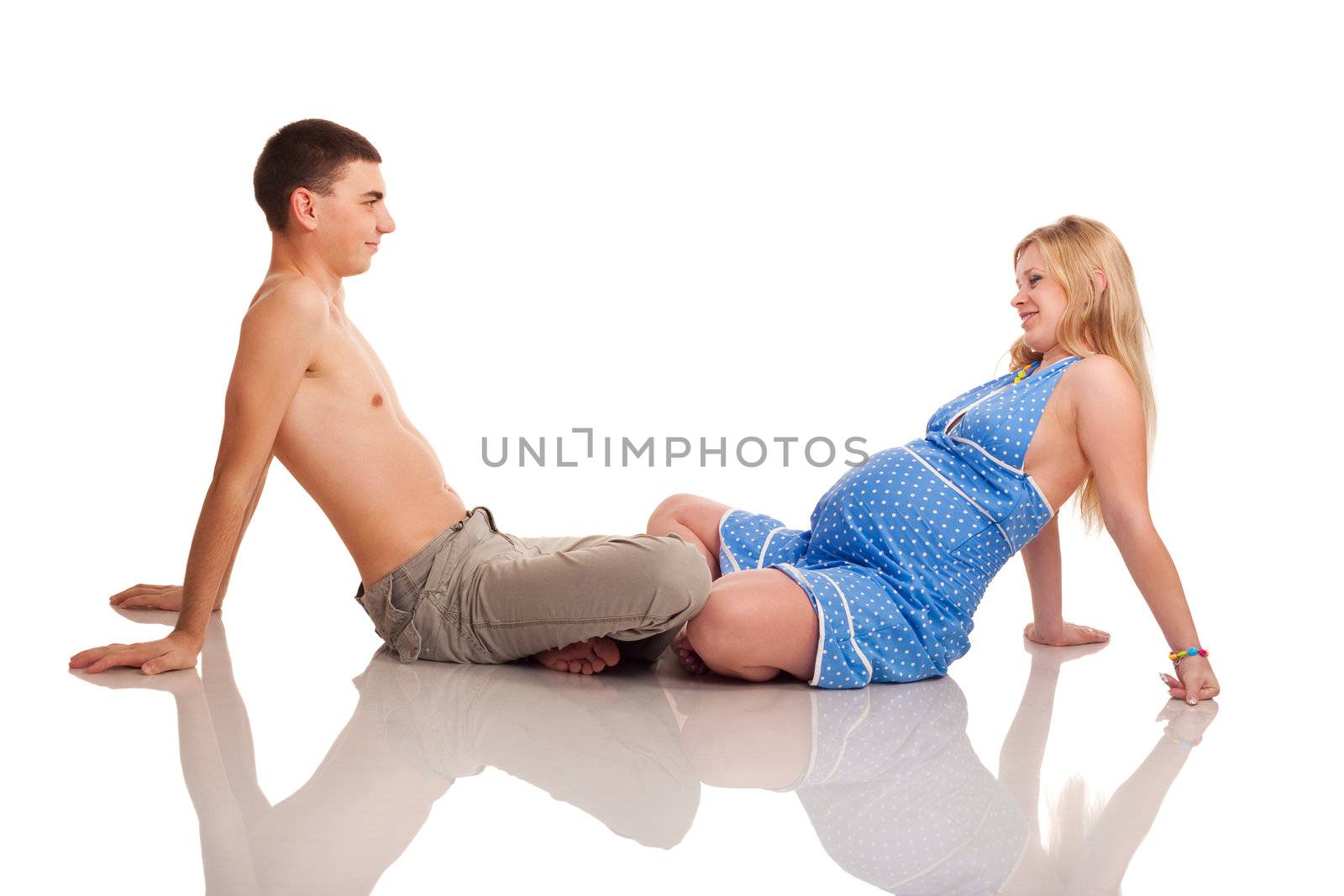 Pregnant woman with her husband sitting on the floor and looking on each other. Studio shoot on white.