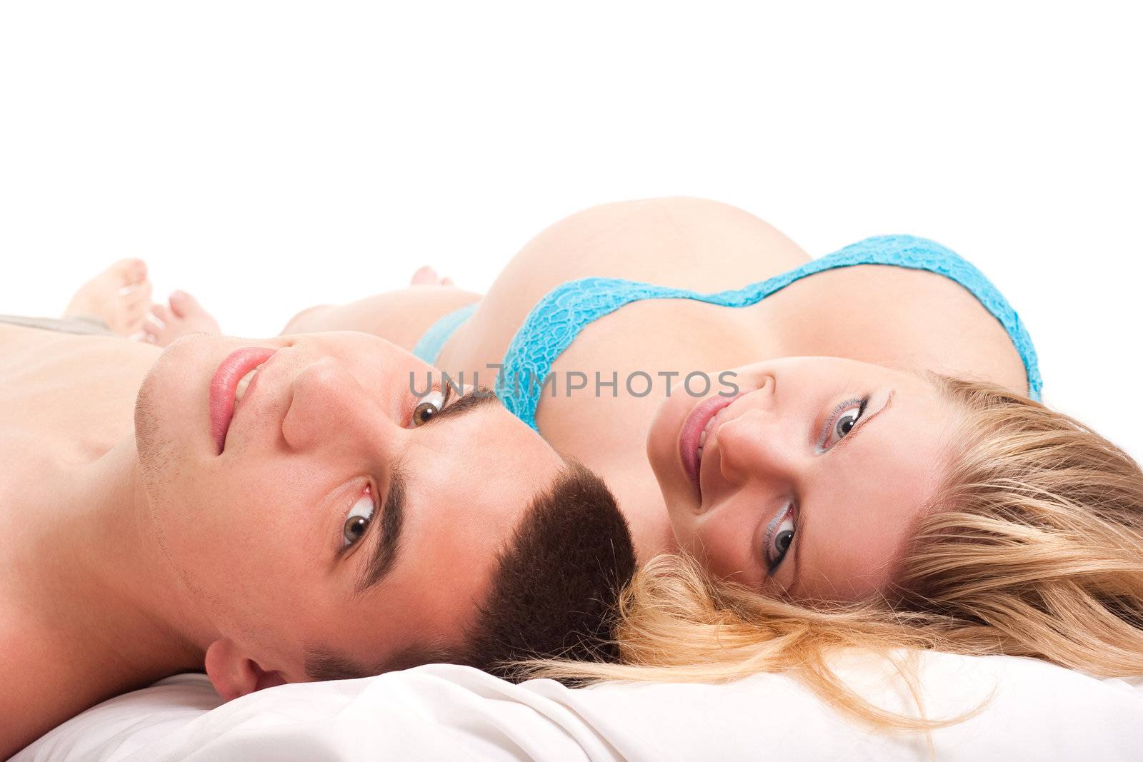 Pregnant woman with her husband laying on white and smiling. Studio shoot on white.