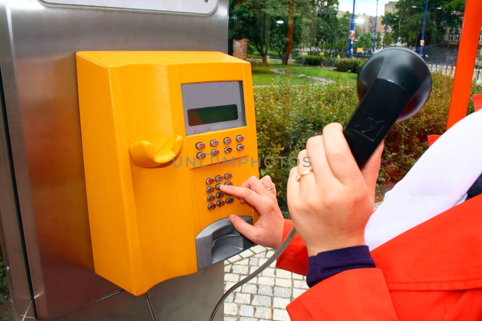 Woman in orange suit is making a call using the yellow public telephone