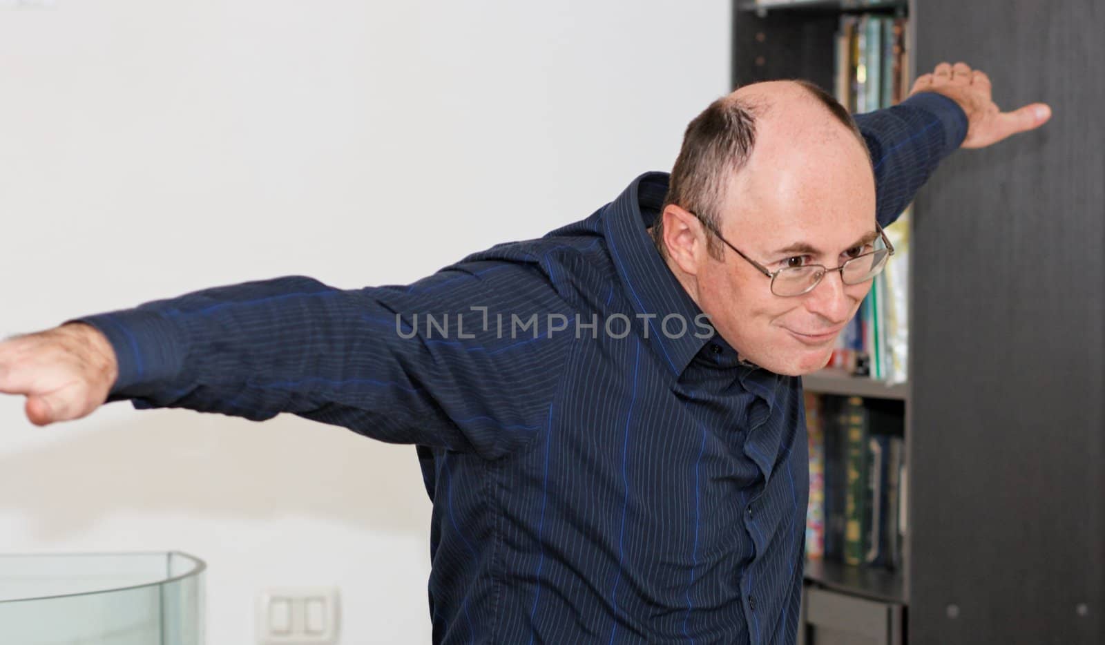 Bald man in glasses spreads his arms as if flying