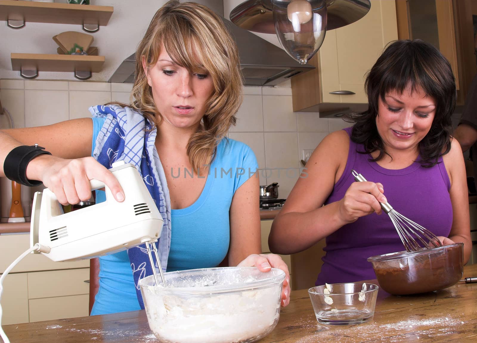 Two sisters busy in the kitchen making brownies and cake