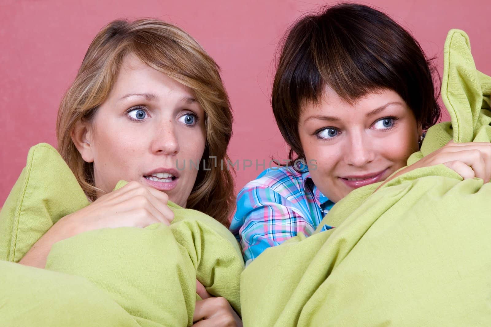 Two girl watching a scary movie while hugging their pillows for comfort