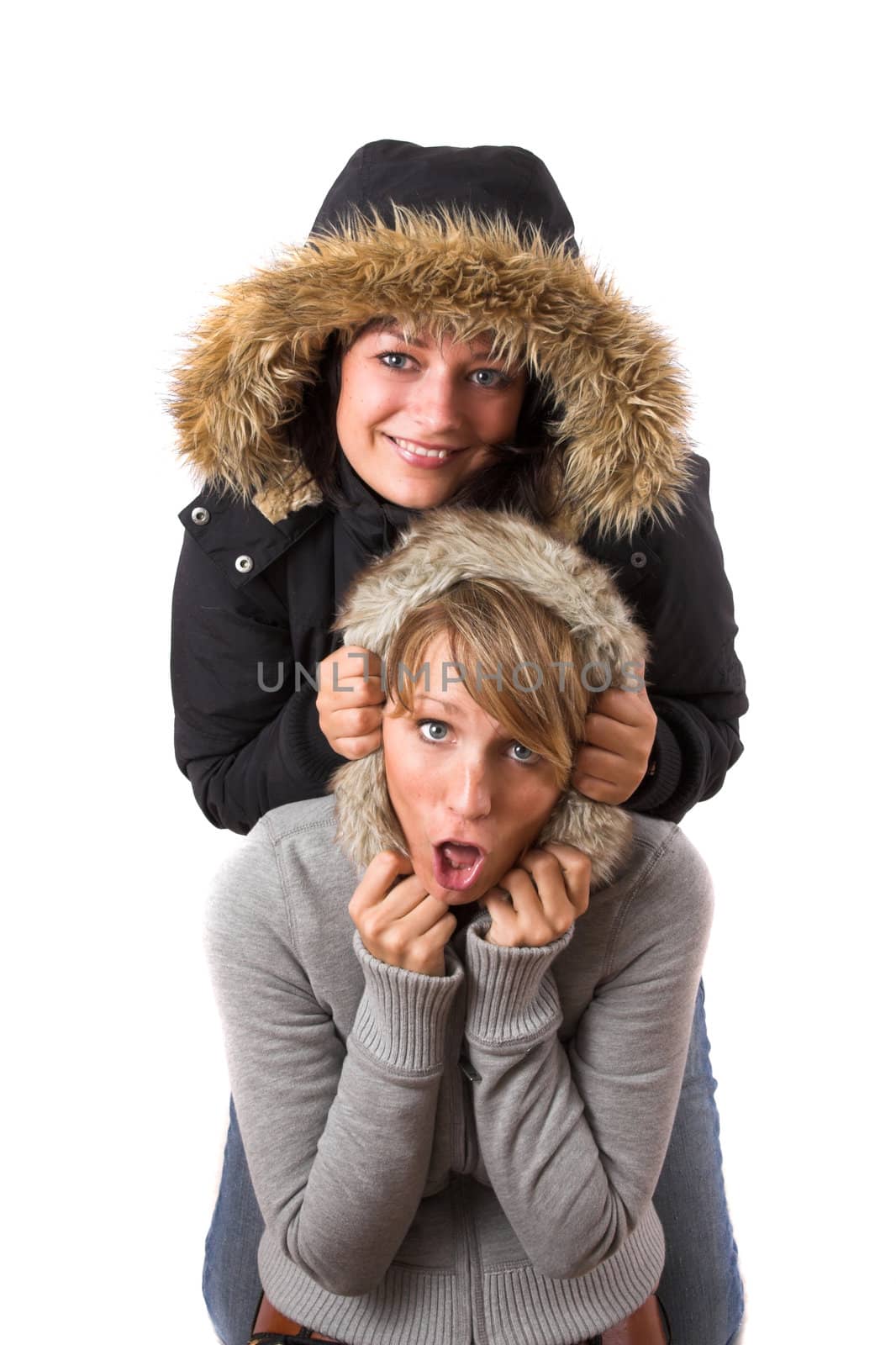 Two sisters posing together in winterjackets while one pulls the hood over the others head