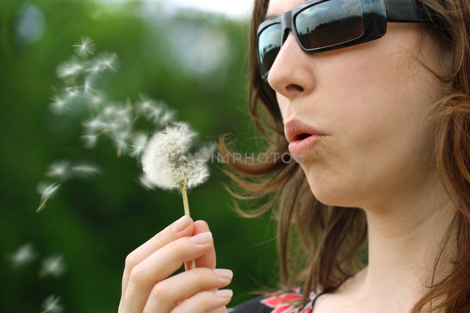 Beautiful female blowing the seeds of a Dandelion into the wind. Shallow depth of field with the focus on her mouth and centre of flower.
