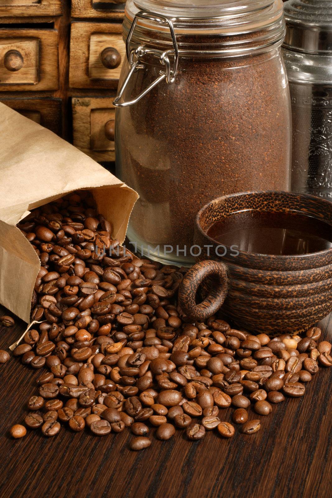 Image of roasted coffee beans, coffee cup, and ground beans on a wooden table.

