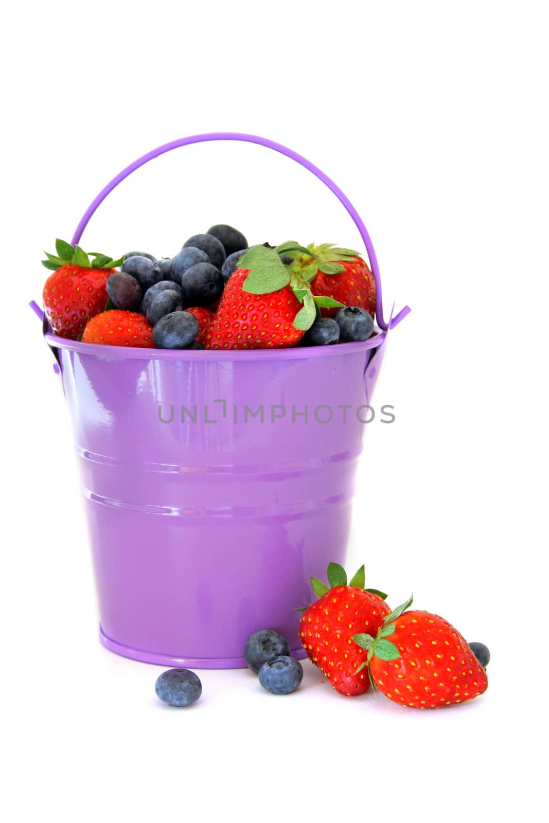 A purple bucket full of blueberries and strawberries spilling over. All isolated on a white background.